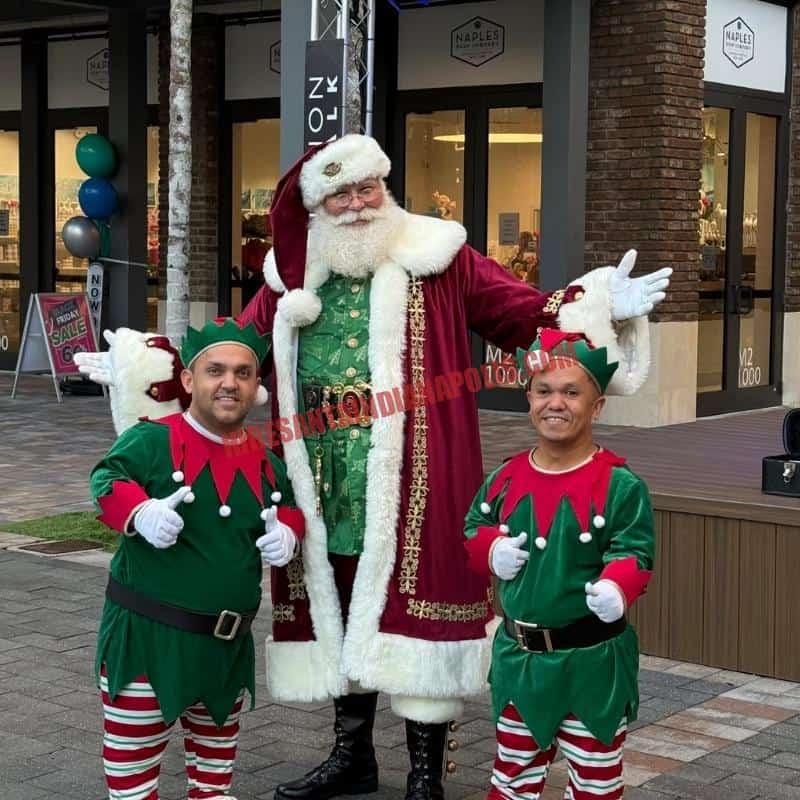 Santa Claus impersonator for hire in Indianapolis standing outdoors with two elves, thumbs up.