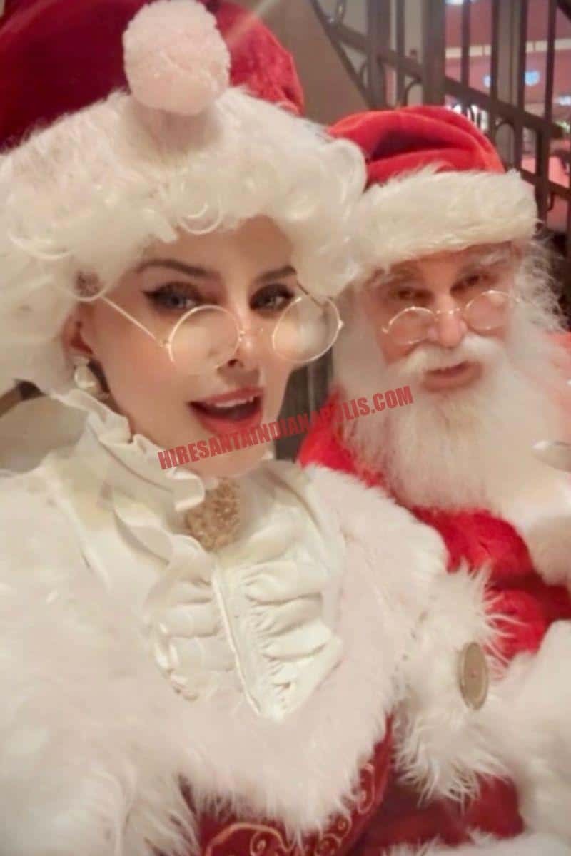 Hire a Santa near you in Indianapolis: Mrs. Claus in white ruffles beside Santa in a red suit.
